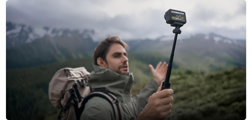 photograph of male hiker walking in mountain side with DJI Osmo Action 5 pro on selfie stick