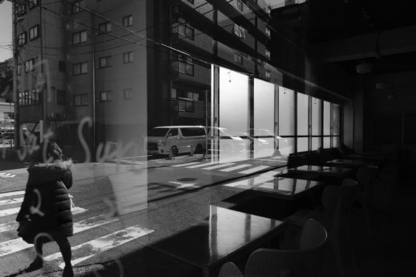 XF16mm f2.8 black and white sample image looking out through japanese cafe window towards tokyo street with woman crossing the road