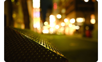 Photograph of knurled city ledge at night with cityscape lights in blurred round bokeh in the background