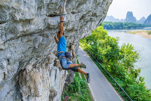 photograph of male rock climber hanging from cliff face above a road