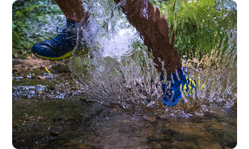 person running through stream creating large water splash comping towards the lens
