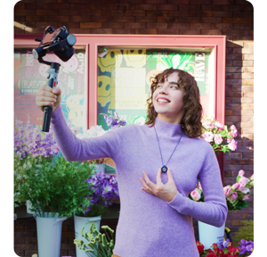 woman wearing purple jumper and lark M2 microphone holding camera and gimbal