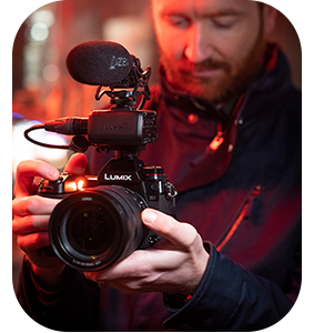 Filmmaker holding Lumix S1RM with Microphone under a red light glow