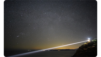 Sony FE 24mm F1.4 GM sample image of lighthouse looking out over ocean bay at night with star filled night sky 