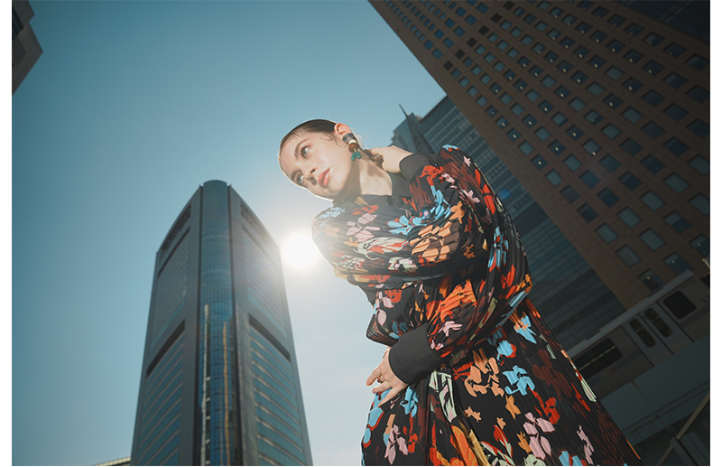 Sony FE 24mm F1.4 GM Lens sample of woman wearing vibrant flowery dress standing between tall skyscraper buildings with clear blue sky