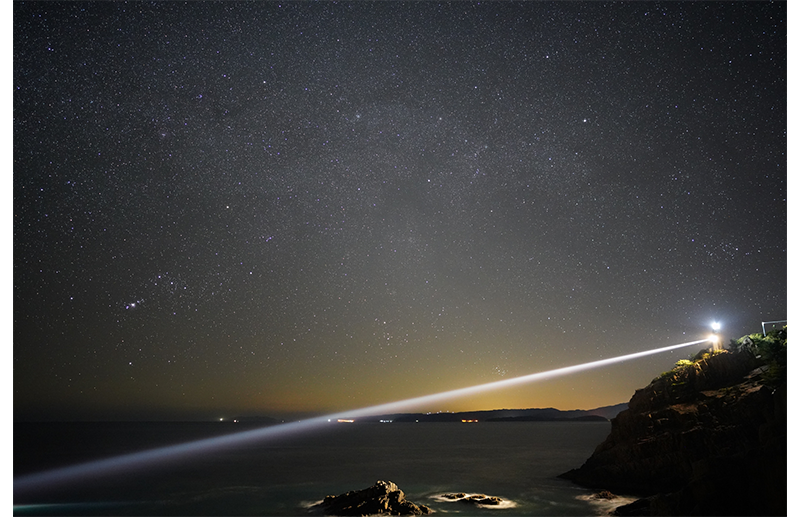 Sony FE 24mm F1.4 GM sample image of lighthouse looking out over ocean bay at night with star filled night sky 