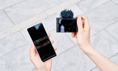 someone holding the sony zv 1 ii compact camera and smartphone